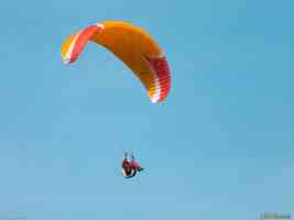 orange paraglider in clear blue sky
